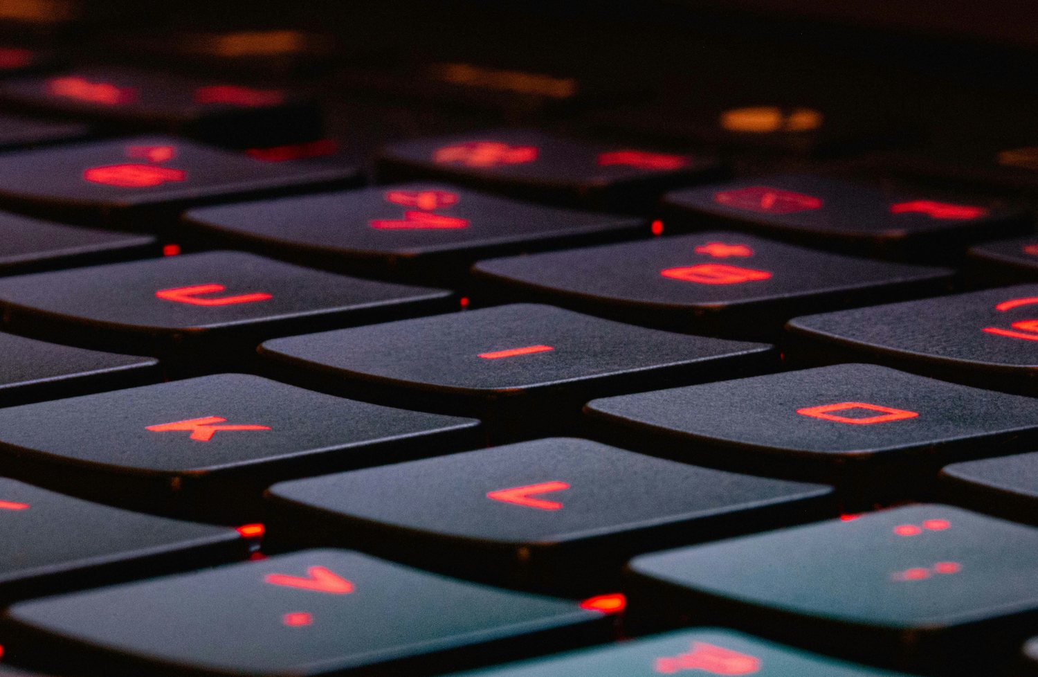 Close-up of a dark keyboard lit from beneath, its key legends glowing red in a dim room