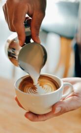 A person pouring milk into a cup of coffee