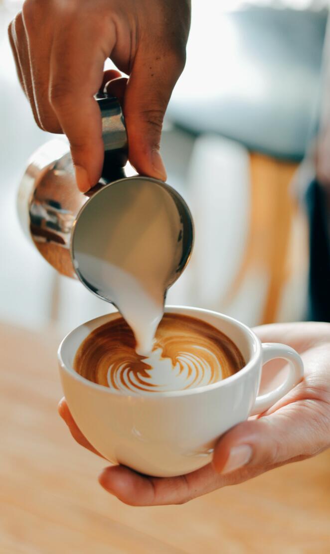 A person pouring milk into a cup of coffee